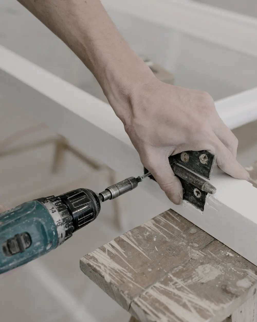 Cordless drill driving a screw into a door hinge