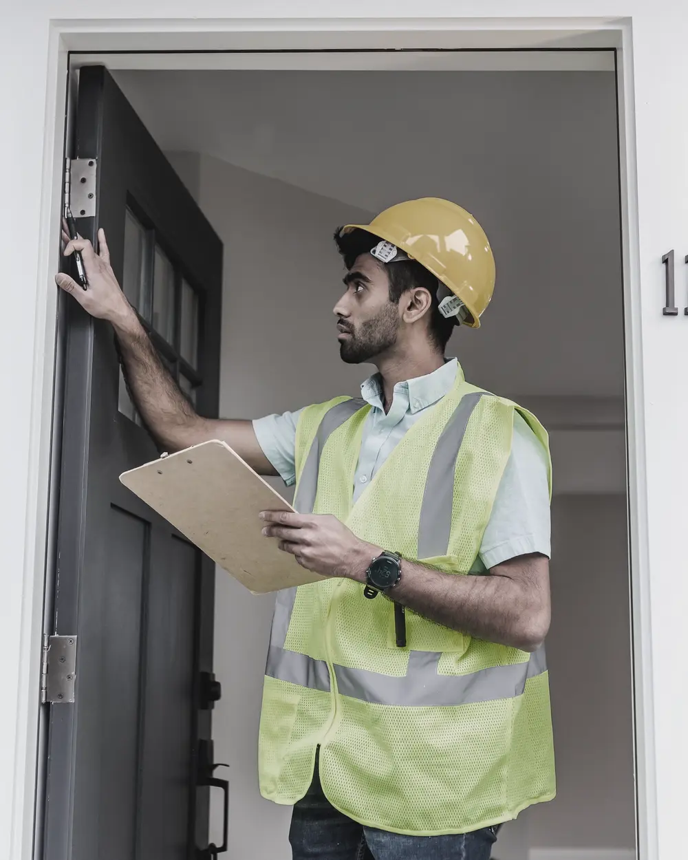 Inspector in a hard hat and safety vest checking a door hinge